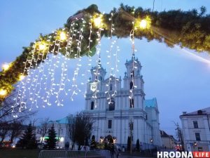 Як у Гродне будуць працаваць паліклінікі, рынкі і гандлёвыя цэнтры ў святы Царква з упрыгожанымі фасадамі прыгожа стаіць за асветленымі падвеснымі агнямі на святочнай арцы, нагадваючы пра ажыўленую атмасферу шумных рынкаў.