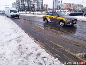 Як зэканоміць на таксі ў навагоднюю ноч Па заснежанай вуліцы з бруднай слотай праязджаюць машыны і зрэдку таксі, а на заднім плане вымалёўваюцца жылыя дамы. Гэта сцэна, якая адлюстроўвае кіпучую энергію навагодняй ночы.